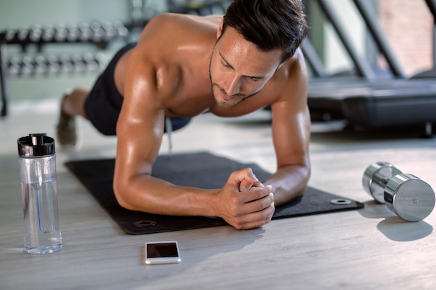 Gespierde atleet die traint in plankhouding tijdens crosstraining bij healthclub