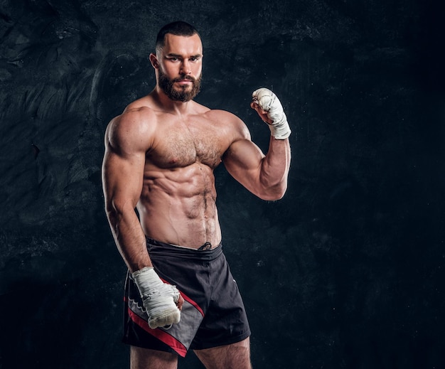 Gespierde knappe vechter met naakte torso demonstreert zijn kracht in een donkere fotostudio.