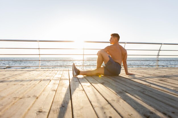 Gespierde man die asana-yoga beoefent om de spieren te strekken bij zonsopgang op het strand