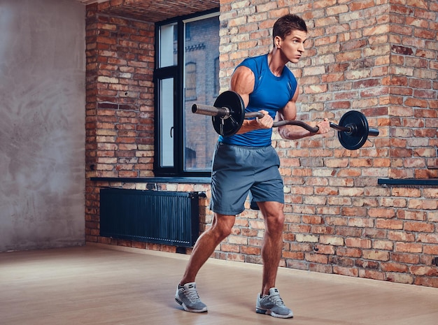 Gespierde man doet biceps-oefeningen met barbell in een club met loft-interieur.