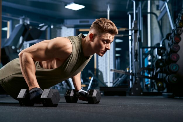 Gespierde man doet push-ups met behulp van halters.