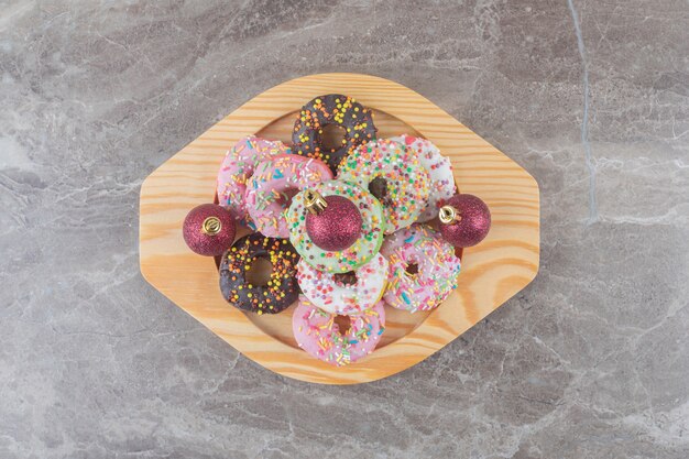 Gestapelde donuts en kerstballen op een houten schotel op marmeren oppervlak