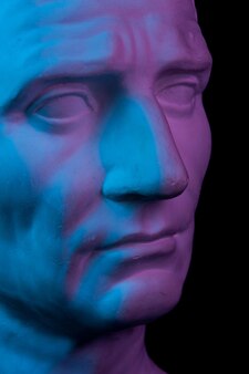 Gestemde gipskopie van oud standbeeld van guy julius caesar octavian augustus hoofd voor kunstenaars op een zwarte achtergrond. gipsen sculptuur van het gezicht van de mens. blauw en roze afgezwakt.