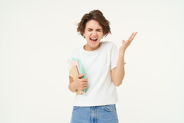 Gestresste jonge studente vrouw schreeuwt stands met notitieboekjes en mappen ziet er depressief uit