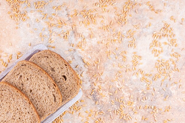 Gestrooid graan naast gesneden brood op een houten plaat, op de marmeren achtergrond.