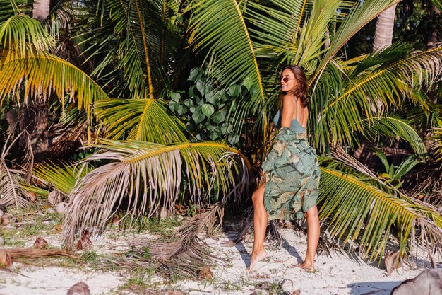 getatoeëerde blanke vrouw in denim shorts en groene trendy crop top op het strand