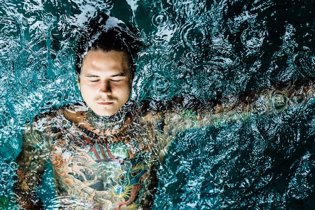 Getatoeëerde man in het zwembad in de regen.