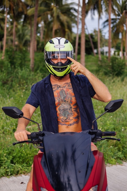 Gratis foto getatoeëerde sterke man op tropische jungle veld met rode motor