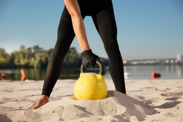 Gratis foto gewas portret van jonge vrouw training met gewichten op het strand