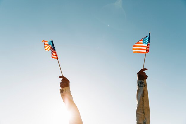 Gewassenvrouw die Amerikaanse vlaggen houden tegen blauwe hemel