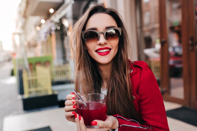 Geweldig meisje in bruine zonnebril thee met glimlach drinken