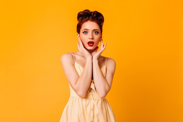 Geweldig pinup meisje poseren in schattige jurk. Studio shot van knappe gembervrouw geïsoleerd op gele ruimte.