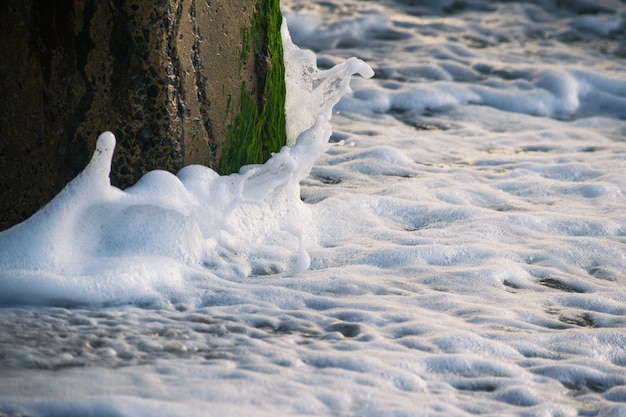 Gratis foto geweldig shot van zeegolven die een stenen kolom raken die bedekt is met mos en spatten maken