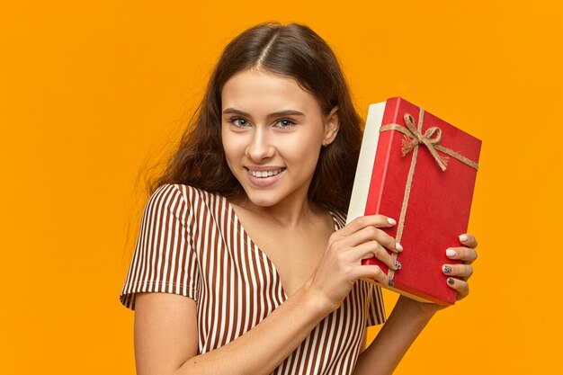 Geweldige emotionele jonge vrouw met brede, vrolijke glimlach poseren in studio met rode doos