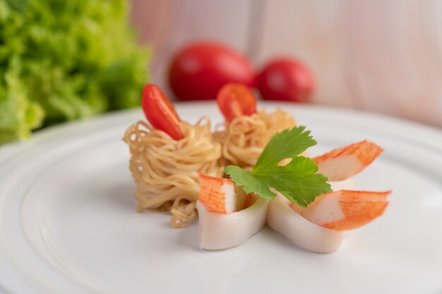 Gewokte instant noodle met garnalen en krabstick in een witte schotel.