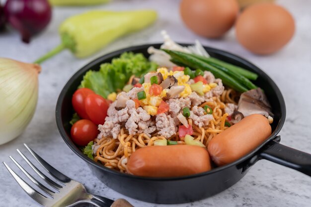 Gewokte noedels met varkensgehakt, edamame, tomaten en champignons in een pan.