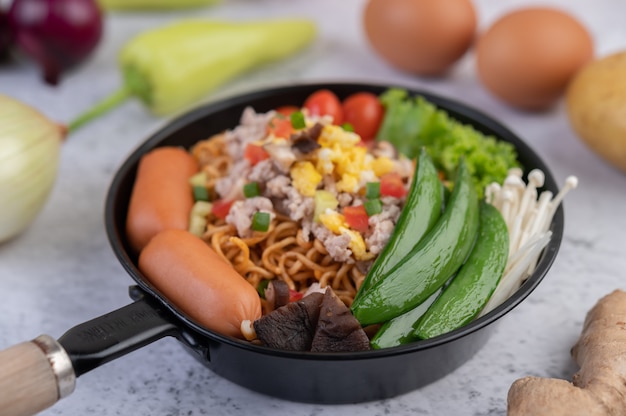 Gewokte noedels met varkensgehakt, edamame, tomaten en champignons in een pan.