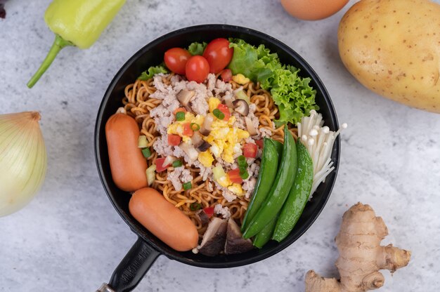 Gewokte noedels met varkensgehakt, edamame, tomaten en champignons in een pan.