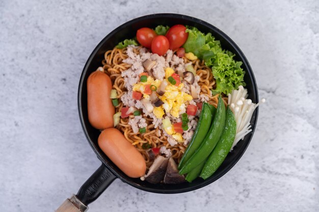 Gewokte noedels met varkensgehakt, edamame, tomaten en champignons in een pan.