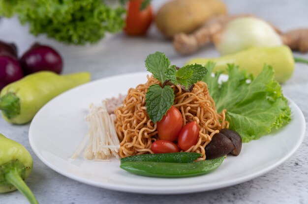 Gewokte noedels met varkensgehakt, edamame, tomaten en champignons in een witte plaat.