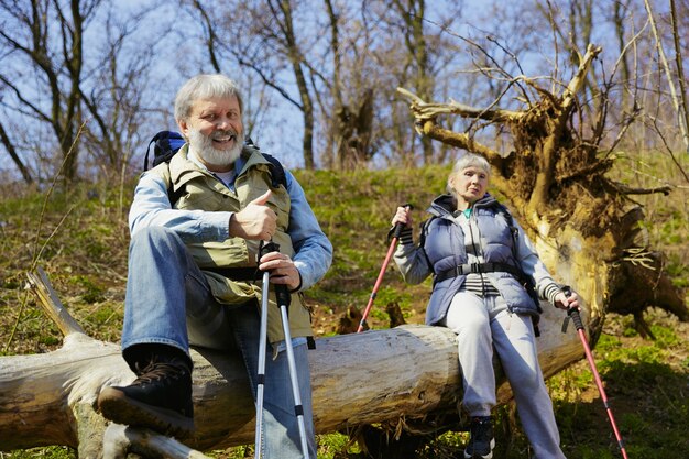 Gezamenlijke rust samen. Leeftijd familie paar man en vrouw in toeristische outfit wandelen op groen gazon in de buurt van bomen in zonnige dag. Concept van toerisme, gezonde levensstijl, ontspanning en saamhorigheid.