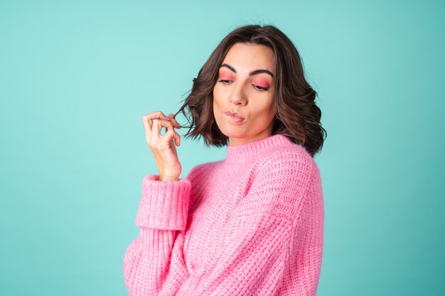 Gezellig portret van een jonge vrouw in een roze gebreide trui en met lichte make-up op turkoois