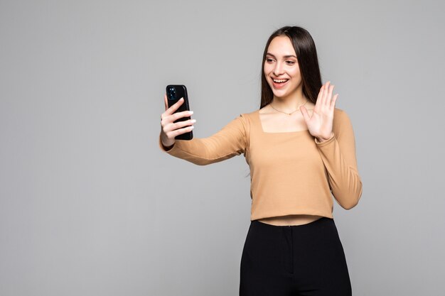 Gezellige mooie vrouw met aziatisch uiterlijk die selfie neemt of een videogesprek voert met behulp van mobiele telefoon geïsoleerd over grijze muur