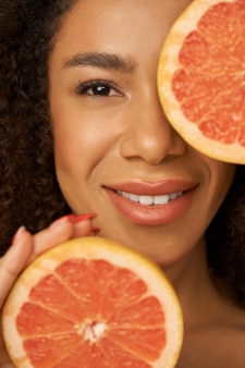 Gezicht close-up van mooie jonge vrouw van gemengd ras die lacht op camera poseren met grapefruit cut