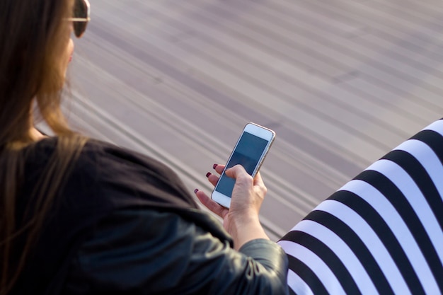 Gezicht op stijlvolle jonge vrouw met behulp van haar mobiele telefoon tijdens het zitten o