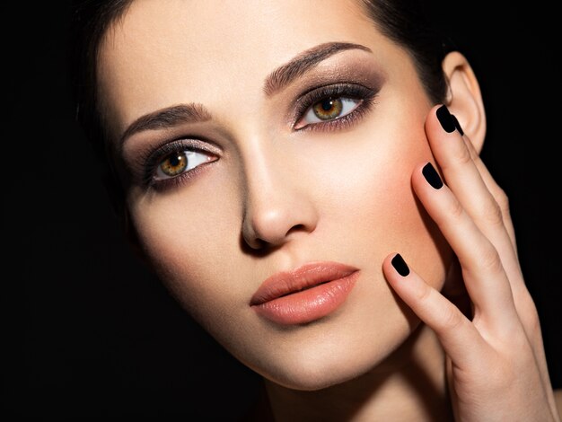 Gezicht van een mooi meisje met mode make-up en zwarte nagels poseren in studio over donkere achtergrond