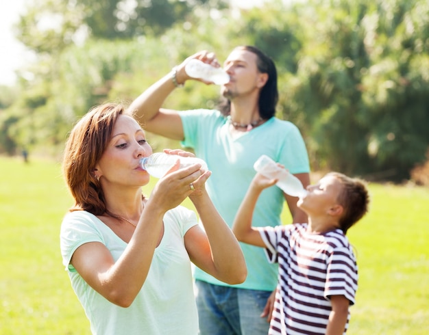 gezin van drie drinken uit plastic flessen