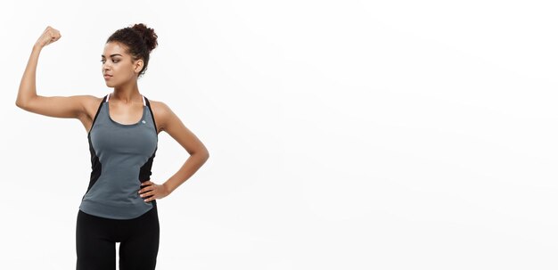 Gezond en Fitness concept Portret van jonge mooie Afrikaanse Amerikaan die haar sterke spier toont met zelfverzekerde vrolijke gezichtsuitdrukking Geïsoleerd op witte studio achtergrond