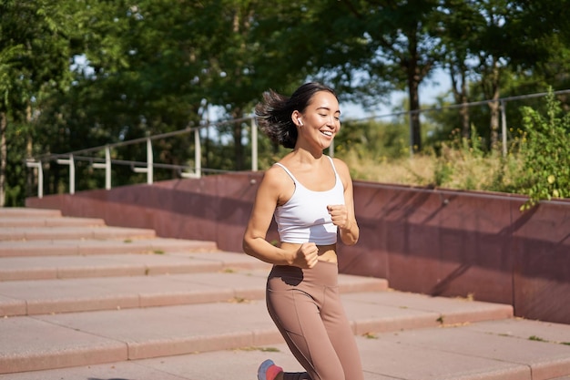 Gezond fitnessmeisje dat buiten op straat loopt en uniform jogt in de frisse lucht en luistert naar m