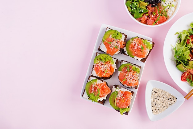 Gezond ontbijt. Boeddha schaal met rijst, mango, avocado en zalm en frisse salade met tomaten, avocado, rucola, zaden, zalm en zalm sandwich met avocado, creame cheese en microgreen. Genezen