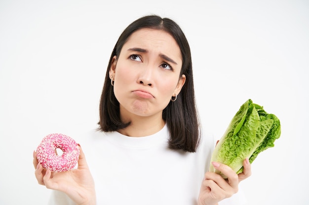 Gezond schoon detox eten concept vegetarisch veganistisch rauw concept verdrietig aziatisch meisje op dieet houdt donut vast