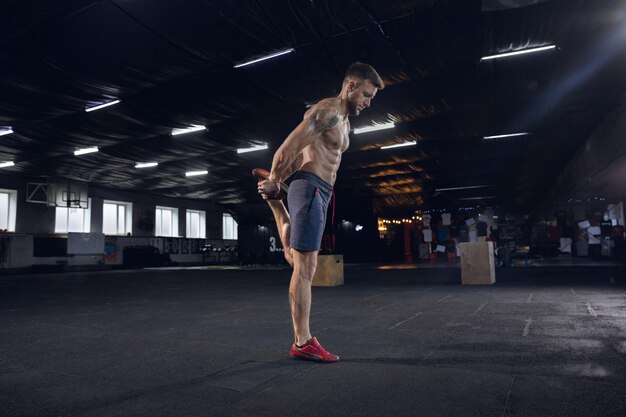 Gezonde jongeman, atleet oefeningen doen, die zich uitstrekt in de sportschool. Enig Kaukasisch model dat hard oefent, zijn lichaam opleidt. Concept van een gezonde levensstijl, sport, fitness, bodybuilding, welzijn.