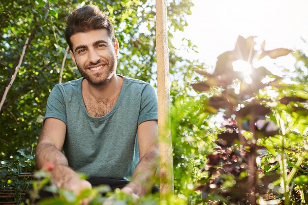 Gezonde levensstijl. Vegetarisch eten. Portret van jonge vrolijke bebaarde blanke man glimlachen, werken in de tuin close-up.