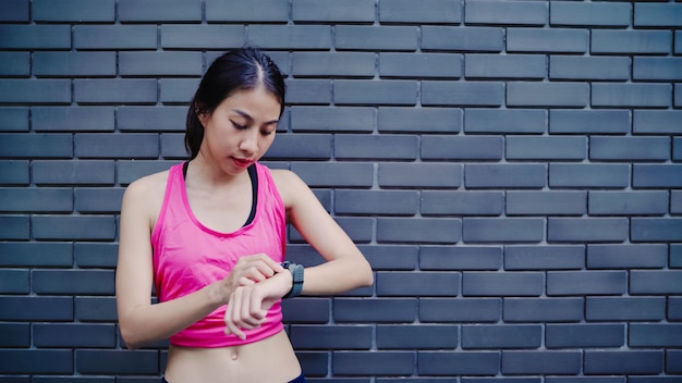 Gezonde mooie jonge aziatische atletenvrouw die en vooruitgang plaatsen die de monitor van het harttarief kijken kijken