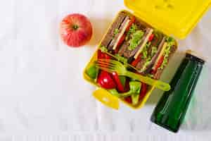 Gratis foto gezonde school lunchbox met rundvlees sandwich en verse groenten, fles water en fruit op witte tafel. bovenaanzicht. plat liggen