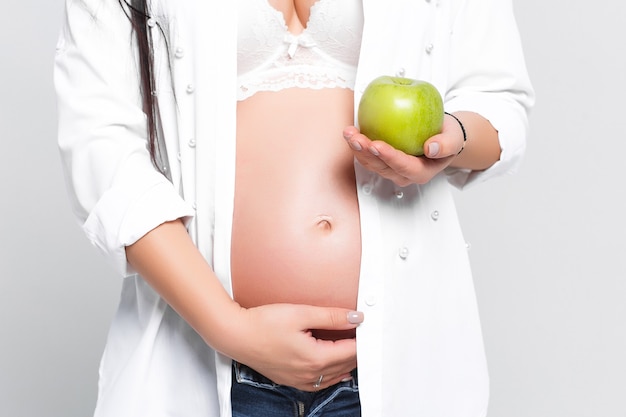 Gezonde zwangere vrouw met vitaminerijke appel die haar buik vasthoudt