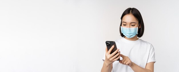 Gezondheid en covid concept jonge aziatische vrouw met medisch masker met behulp van mobiele telefoon typen op smartphone s