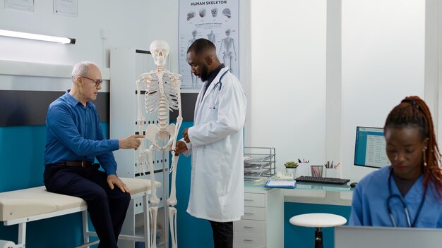 Gezondheidsspecialist die botten van het menselijk skelet in de kast analyseert en de diagnose van osteopathie aan een oudere patiënt uitlegt. Osteopaat die orthopedische anatomie ruggenmerg onderzoekt bij medische afspraak.
