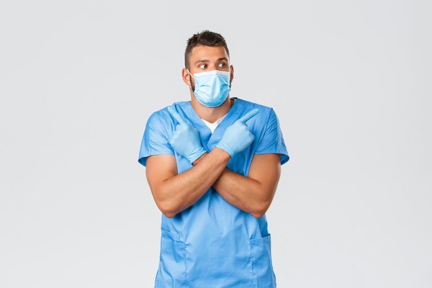 Gezondheidswerkers, covid-19, coronavirus en preventie van virusconcept. Geïntrigeerde en besluiteloze knappe dokter, verpleger in scrubs en medisch masker die keuze maken, zijwaarts wijzend op banners