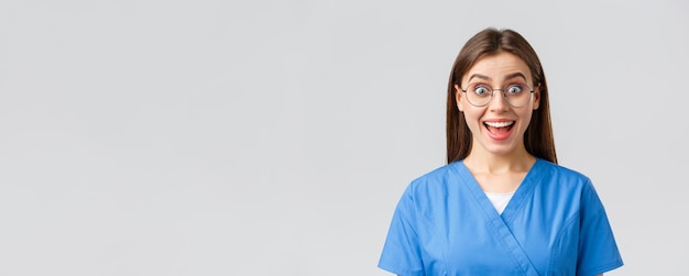 Gezondheidswerkers geneeskunde verzekering en covid19 pandemie concept Enthousiaste vrolijke vrouwelijke verpleegster arts in blauwe scrubs en glazen horen fantastisch nieuws glimlachend geamuseerd