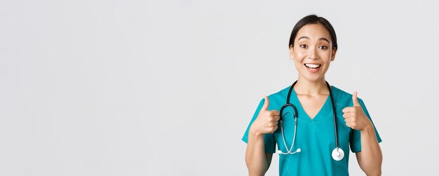 Gezondheidswerkers, het voorkomen van virussen, quarantainecampagneconcept. Jonge ondersteunende Aziatische verpleegster geeft thumbs-up. Dokter cheer-up patiënt, iemand aanmoedigen of compliment, witte achtergrond