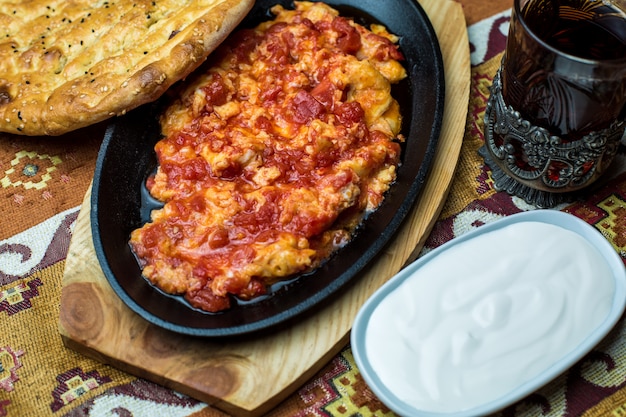 Gietijzeren schotel van ei en tomatenschotel geserveerd met yoghurt en tandoor brood