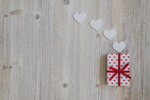 Gift van stippen met rode boog met papieren harten op een houten tafel