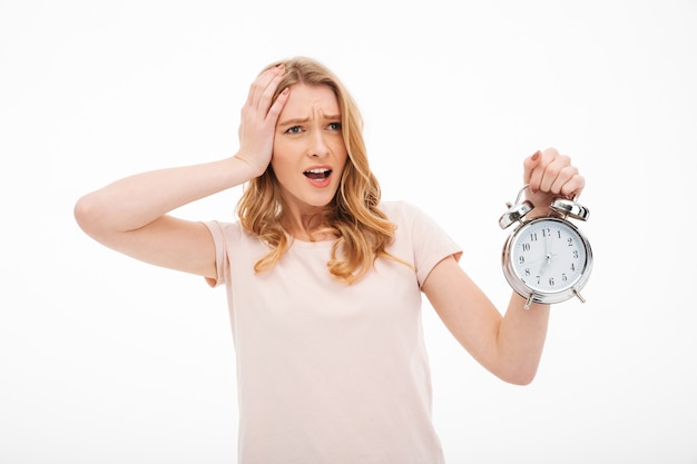 Gillende jonge verwarde vrouw die wekker houdt.