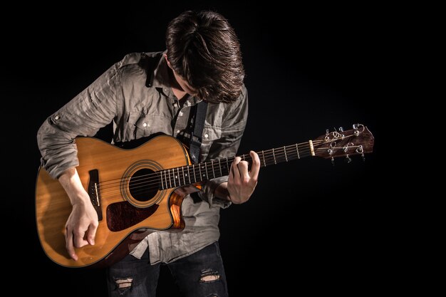 Gitarist, muziek. Een jonge man speelt een akoestische gitaar op een geïsoleerde zwarte achtergrond