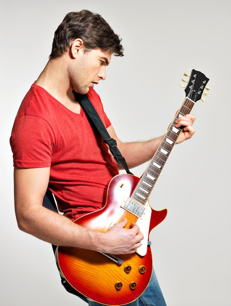 Gratis foto gitarist speelt op de elektrische gitaar met heldere emoties op een grijze achtergrond
